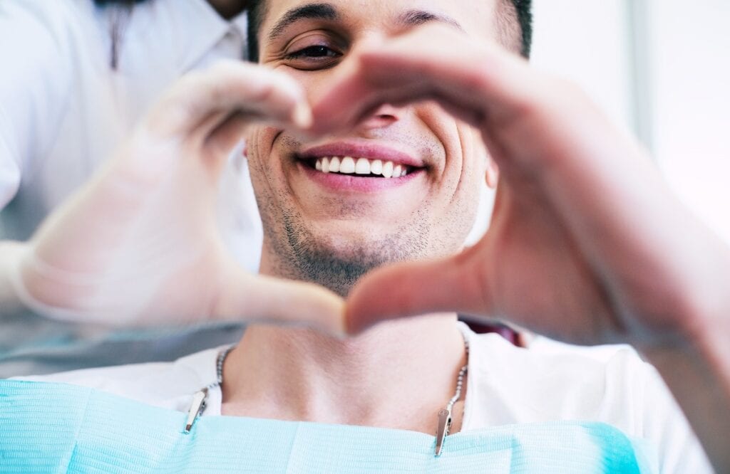 Cheer of heart. A patient with white and healthy smile in the center of a heart made from two hands of a doctor and a patient which is telling about pleasant emotions of the appointment.