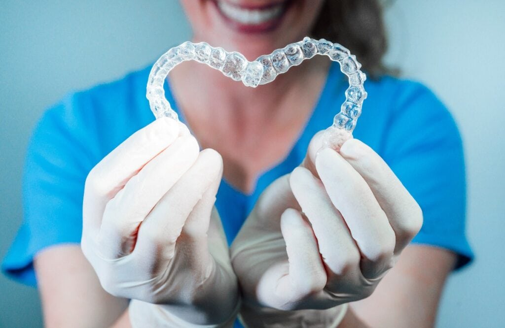 Female doctor holding two transparent heart-shaped dental aligners